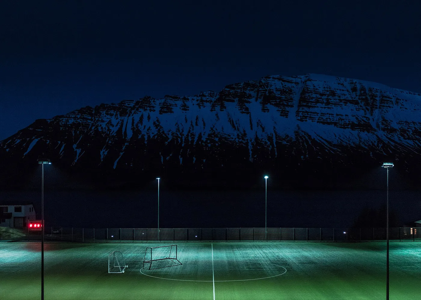 Campo de futebol iluminado por projetores durante a noite, sem jogadores em campo