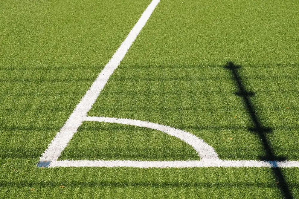 Grande plano da marcação branca do canto de um relvado com a sombra de um poste