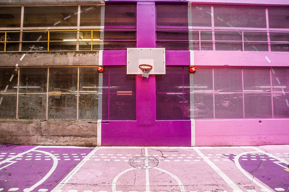 Piso de um recinto desportivo com marcações pintadas em tons claros e uma tabela ao fundo