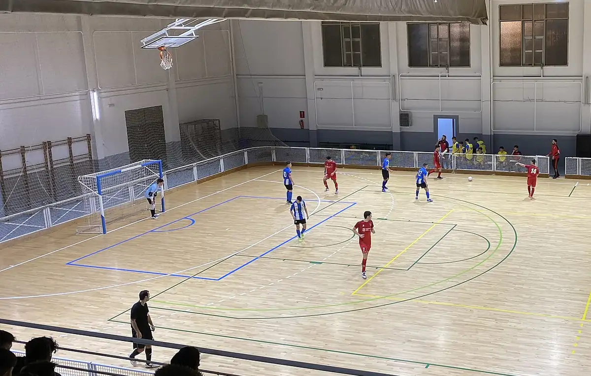 Pavilhão desportivo com piso de madeira, marcações coloridas e uma baliza de futsal
